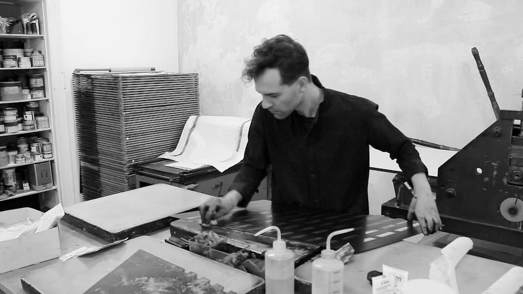 The architect Oliver Siebe, a 30-year-old man with dark hair, stands in the printmaking studio and works with paint on his printing plate.