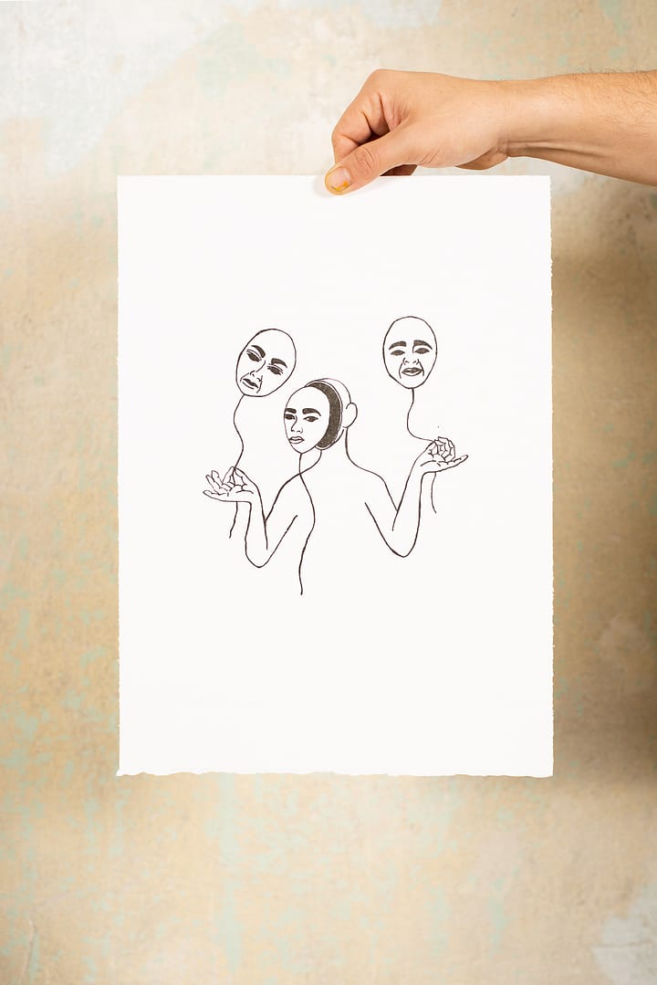 Hand hält lithographische Druckgraphik vor einer Wand. Auf der Graphik ist eine Frau zu sehen, deren Gesicht eine Maske ist. Sie hält zwei Luftballons, deren Körper ebenfalls Frauenmasken ähnelt.